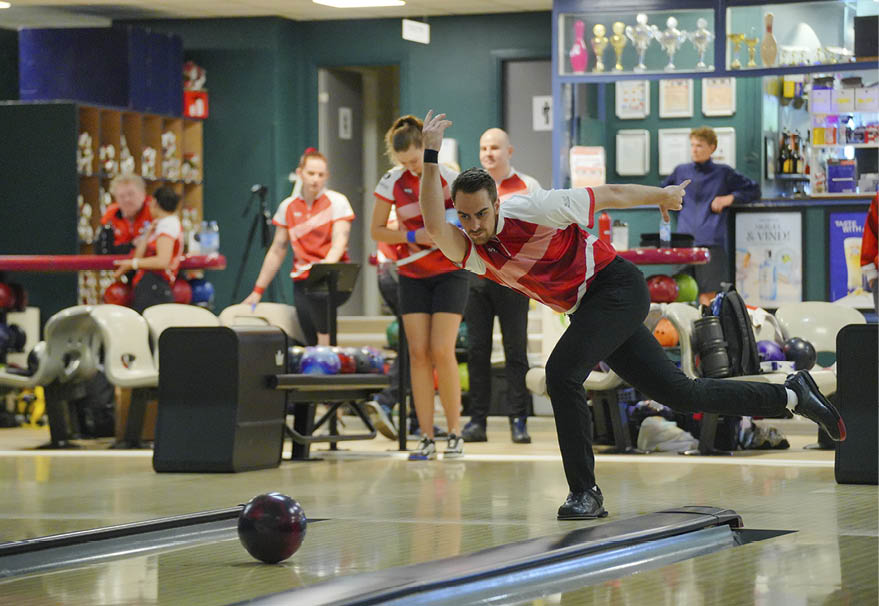 A person wearing a red and white sports jersey is in a bowling alley preparing to roll a bowling ball. Description generated by AI